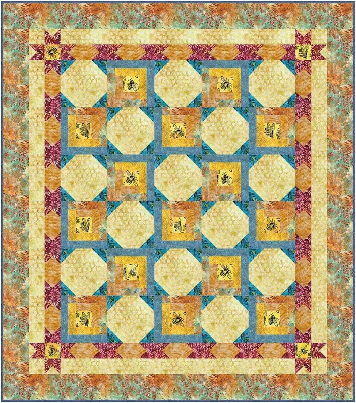 A colorful patchwork quilt with a floral border, blue and orange geometric patterns, and a grid of yellow squares featuring bee illustrations. The quilt has a symmetrical, intricate design.