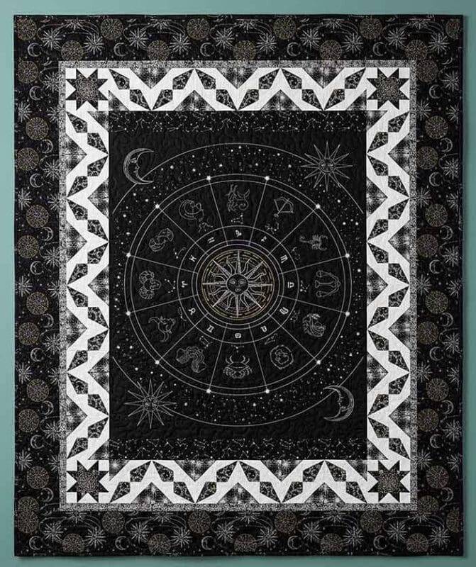 A decorative tapestry featuring a central zodiac wheel with astrological symbols, surrounded by geometric patterns, moons, and stars in black and white. The border is adorned with celestial motifs.