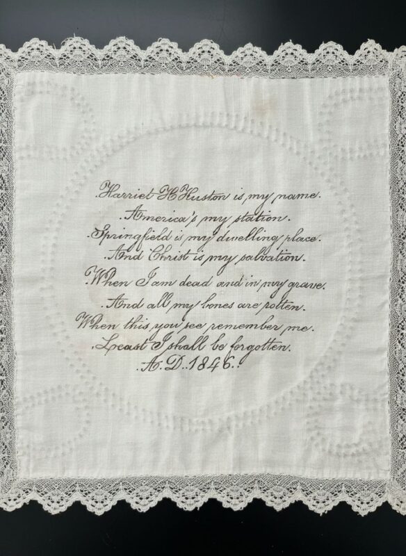 A white handkerchief with lace edges features neat, cursive black embroidery of a religious poem titled Harriet D. Hudson is my name, dated 1846, centered within a circular stitched pattern.