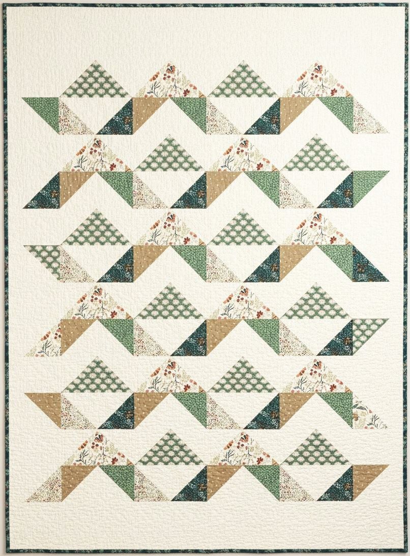 A quilt with a geometric pattern made of triangles and parallelograms in green, beige, floral, and checkered fabrics, arranged in horizontal zigzag rows on a white background.