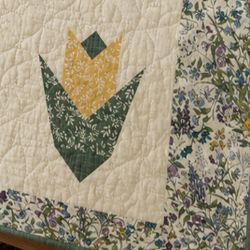 A section of a quilt from the Gem Dandy Lap Quilt Pattern, featuring a stylized yellow and green floral design on a cream background, bordered by fabric with an intricate, colorful floral print.
