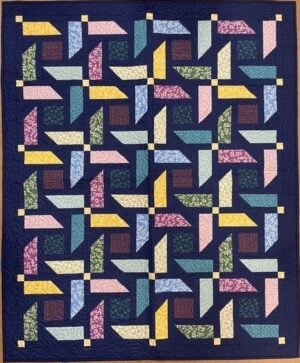 A colorful Turnabout Lap Quilt Pattern featuring a geometric pinwheel design. Various fabric strips in pink, yellow, blue, green, lavender, and red create interlocking shapes on a dark blue background with small yellow squares.