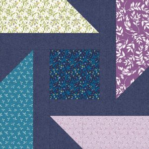 A geometric quilt block pattern with navy blue fabric and four floral print sections in green, purple, teal, and pink, arranged around a central blue square with a leafy design.