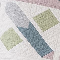 A quilt with geometric shapes, including two green squares and overlapping blue, lavender, and light pink rectangles, all on a white background with diagonal quilted stitching—perfectly embodying the playful style of the Quack Quack Throw Quilt Pattern.