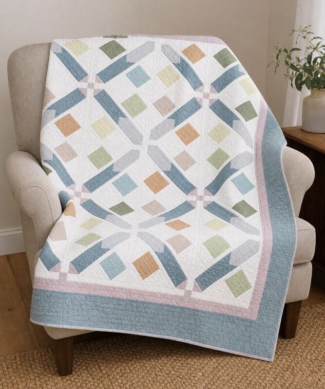 A pastel patchwork quilt with a geometric diamond pattern draped over a beige armchair in a cozy room, next to a small wooden side table with a potted plant.