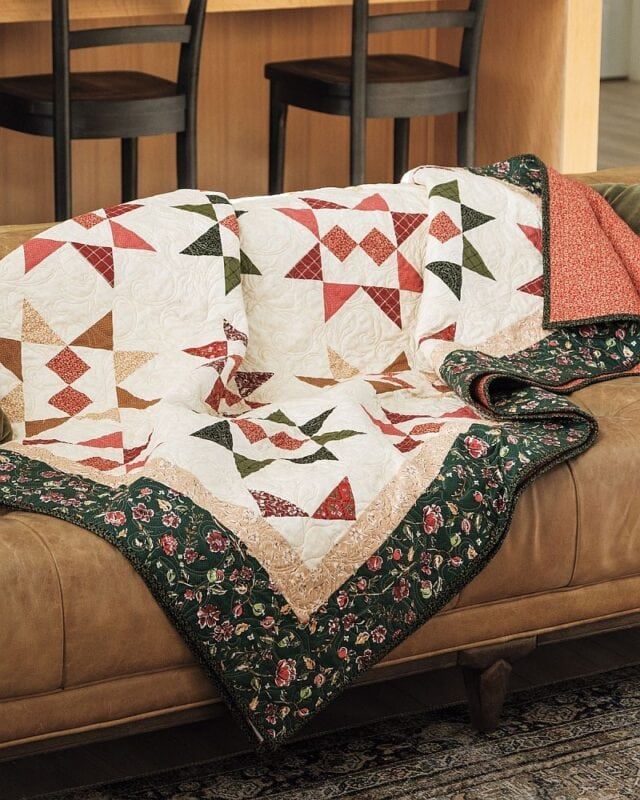 Cider and Cloves quilt draped over a brown leather sofa, showing the star blocks and green floral border