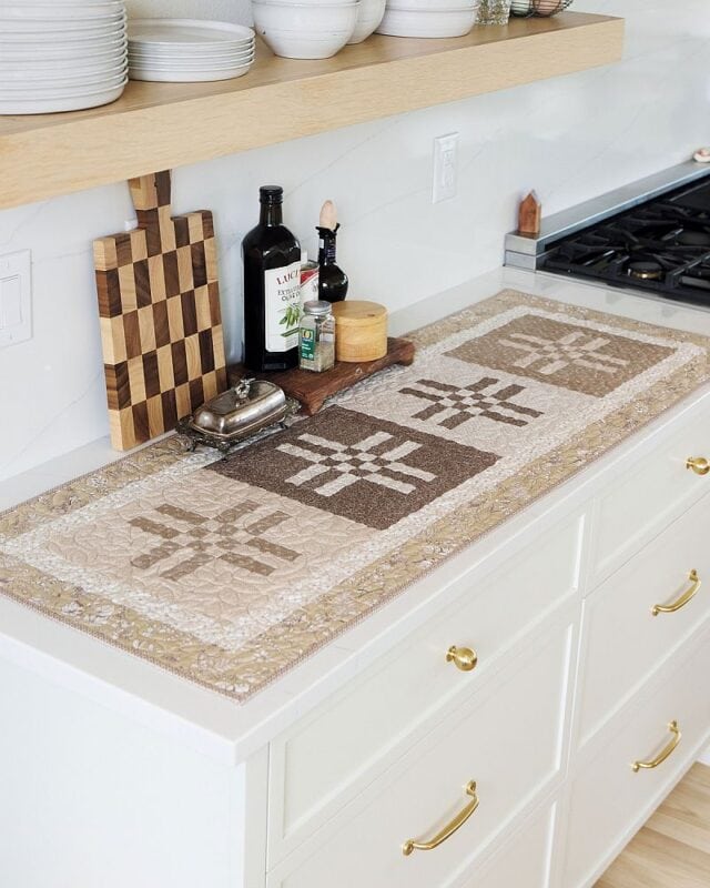 Crossroads Table Runner on a white kitchen counter beside a wooden cutting board, olive oil, and a butter dish